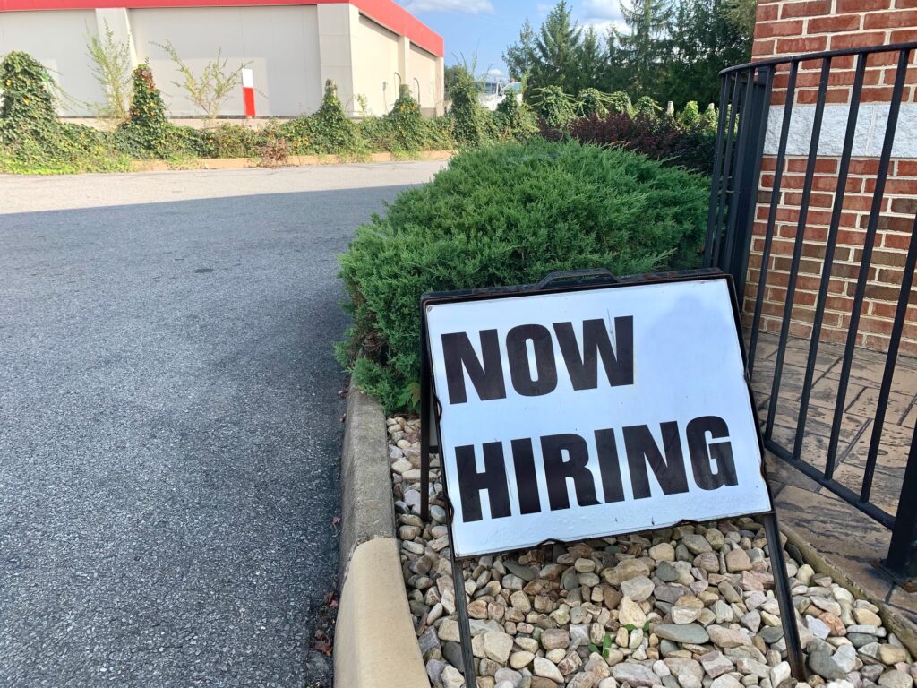 A “Now Hiring” sign at the business entrance since they are returning to work during Covid19